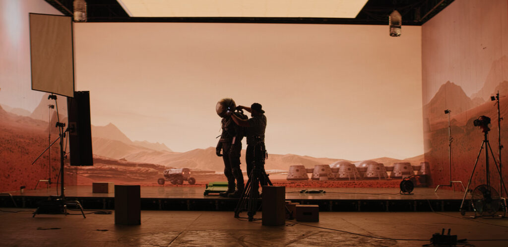 Behind the scenes shot of virtual production stage with huge LED screens, cinematorgapher shooting Mars scene. Future of movie production
