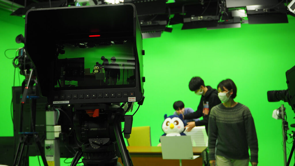 Meiji University production studio with students assembling props before a green screen and camera