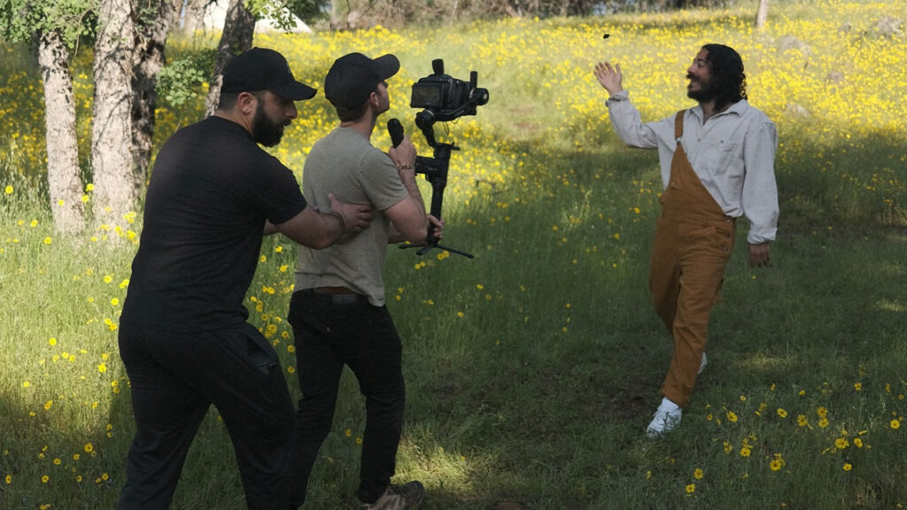 two men operate the Pocket Cinema Camera 6K Pro while filming a man in overalls walk through a field in production on Sunny Day
