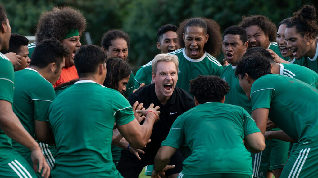 Scene from Next Goal Wins with soccer team in green shirts getting excited on the field