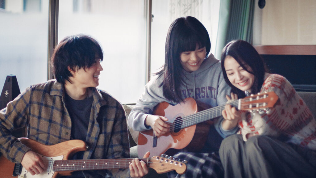 Scene from KYRIE with two women and one man playing guitars