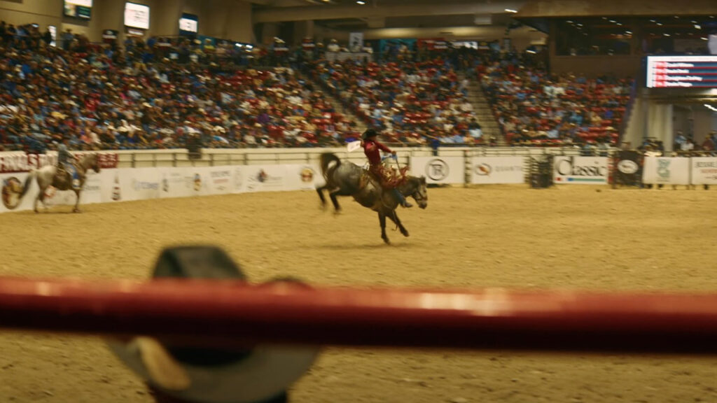 A person rides a bucking horse in a rodeo arena