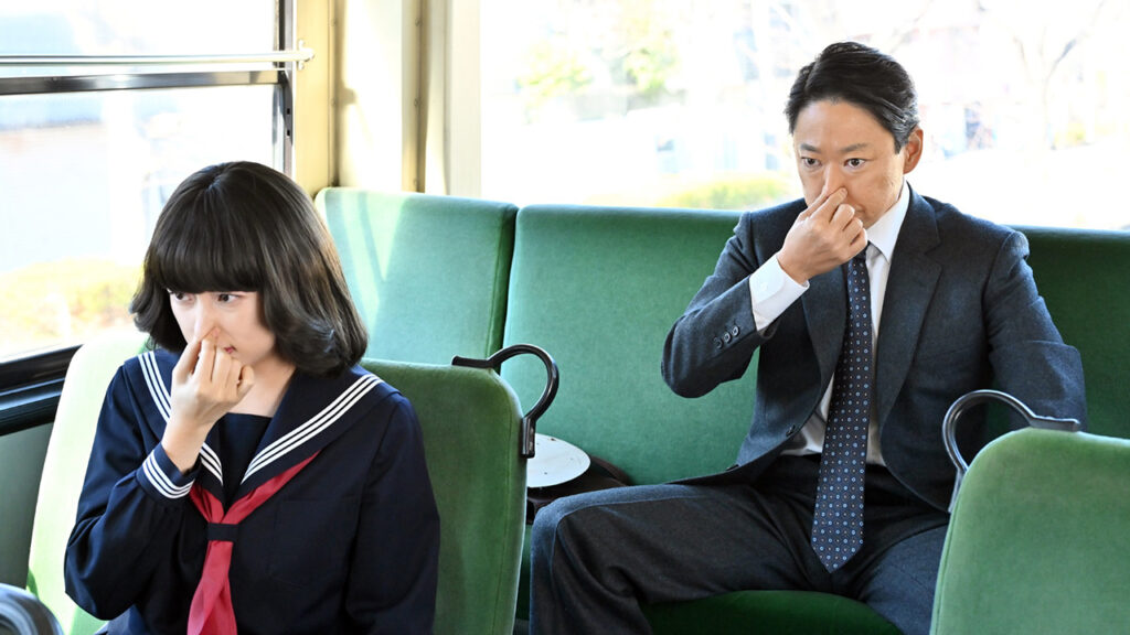 Two people sitting in green seats hold their noses