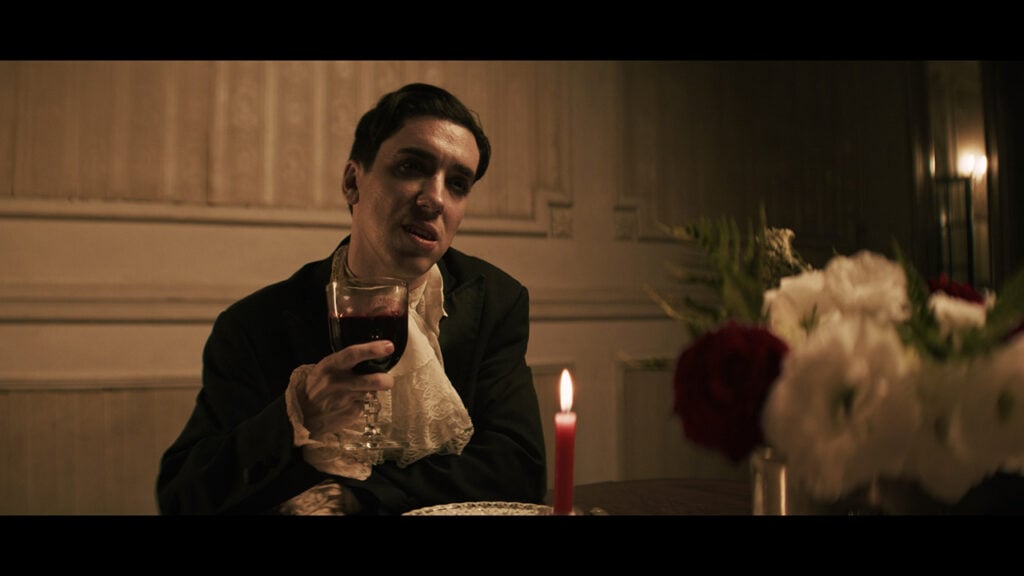 A man sings while wearing a suit and holding a glass of wine in a music video