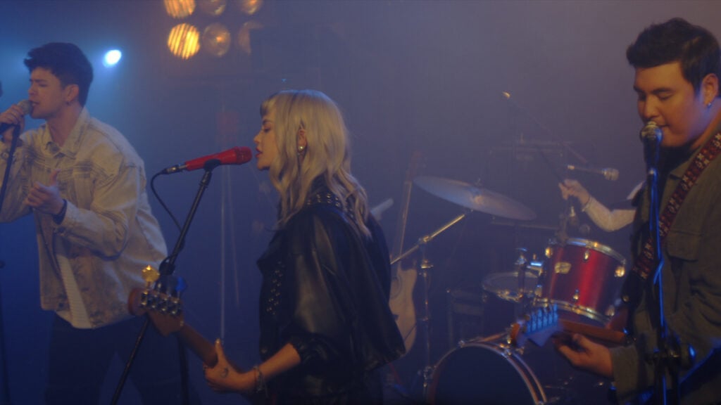 three people sing and play instruments in a band