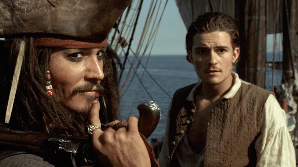 Jack Sparrow smiles while talking to Will Turner on board a ship in the Disney movie Pirates of the Caribbean
