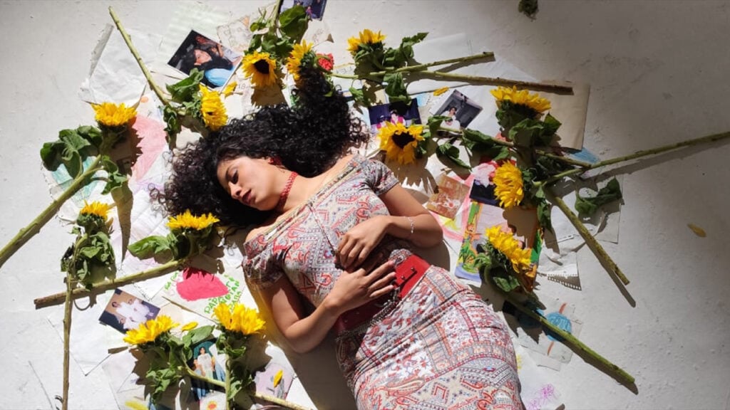 Steffie Beltt lays on the ground amongst sunflowers and childhood art