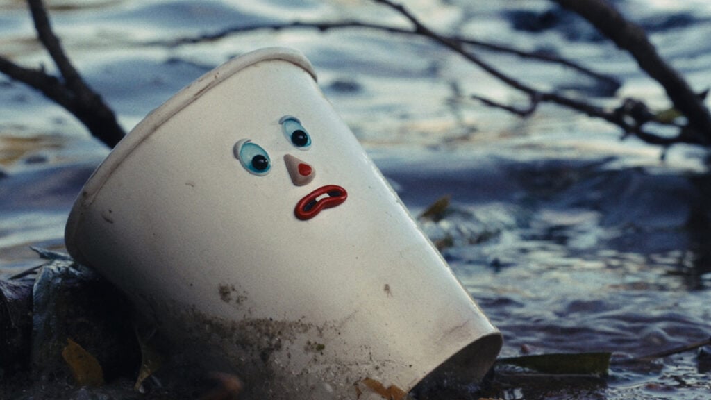 A paper cup with human-like eyes, nose and mouth floats in water