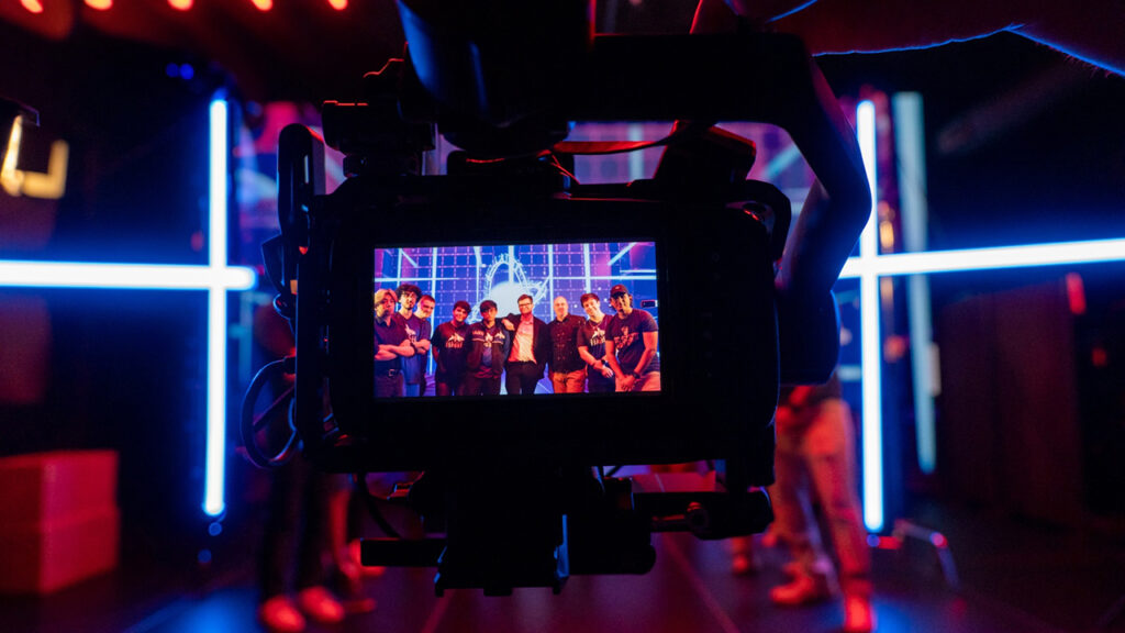 the monitor of a Blackmagic camera shows a display of a group of people posing in front of a light display
