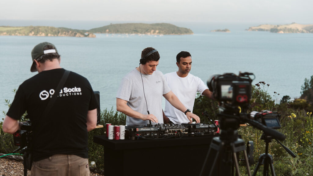 Two DJs mix music next to a beach while a Blackmagic camera films them