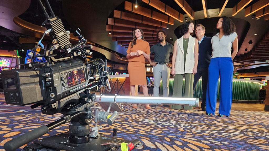 Three women and two men pose before a Blackmagic camera on a casino floor