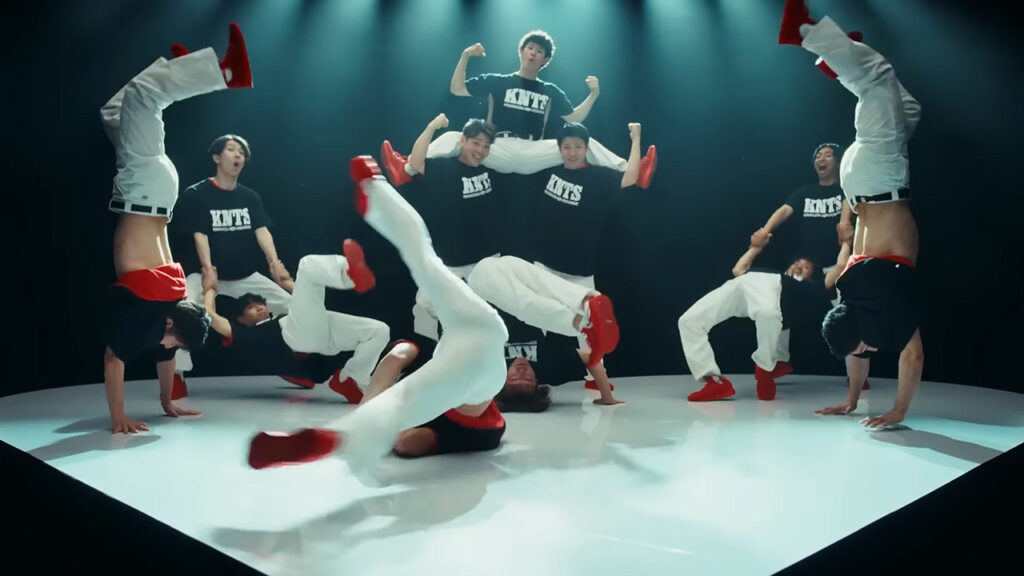 11 men do gymnastics while wearing shirts that say KNTS