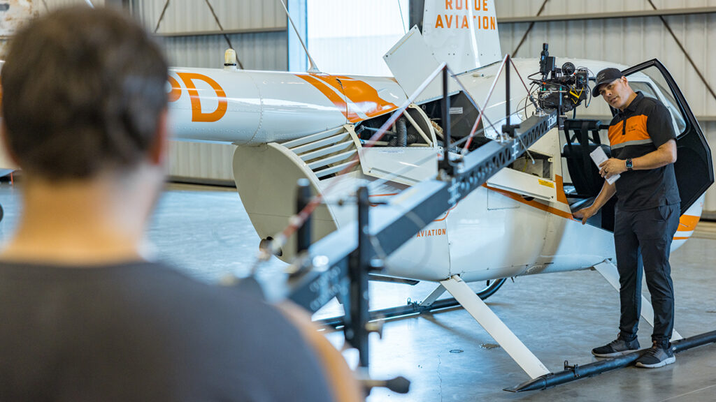 a man talks into a Blackmagic URSA Cine camera while standing in front of a helicopter