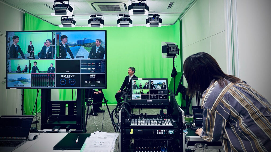 A woman checks the production gear while a man is being filmed in front of a green screen