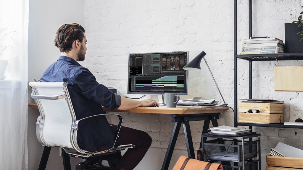 a man edits video at a desk that displays Avid software on the computer screen