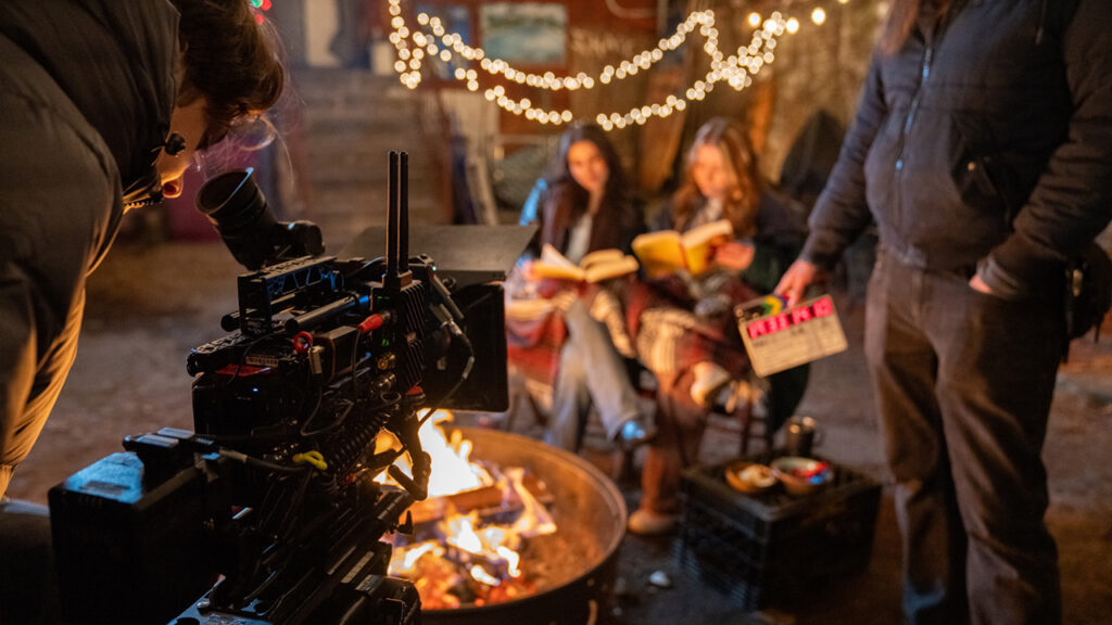 a cameraman films two women sitting in front of a fire