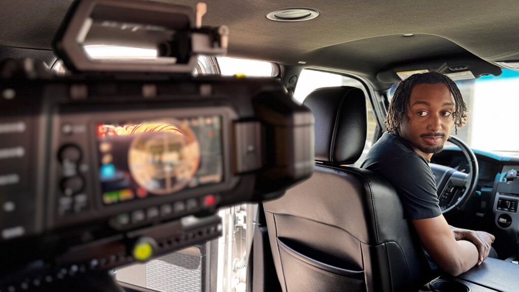 A man sits in the front seat and looks back at the Blackmagic camera filming him from the back seat