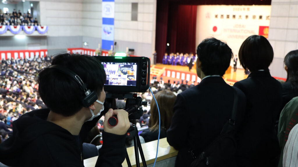 a student runs a camera while filming a large assembly at Jose International University