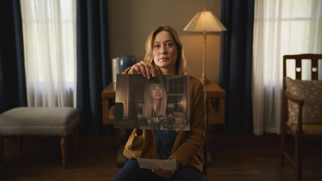 A scene from Shelby Oaks where a woman sits on a chair and holds up a picture of another woman