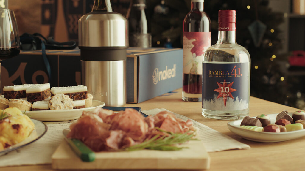 a countertop is spread with wine, gin, chocolates, cookies, and deli meat