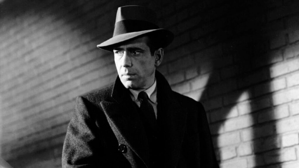 Humphry Bogart wears a fedora and a trench coat in a scene from the movie The Maltese Falcon