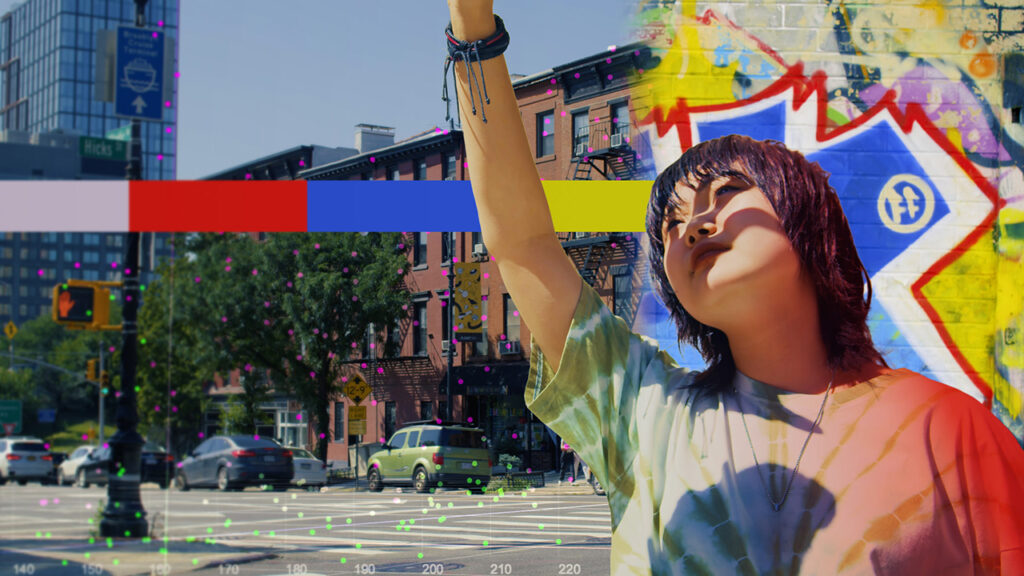 A young girl wearing a tie-dye shirt holds her hand up to block the sun