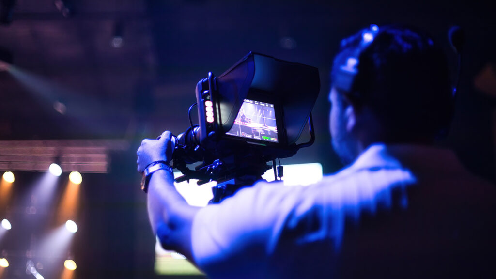 a man checks the viewfinder on a Blackmagic camera on a dark set