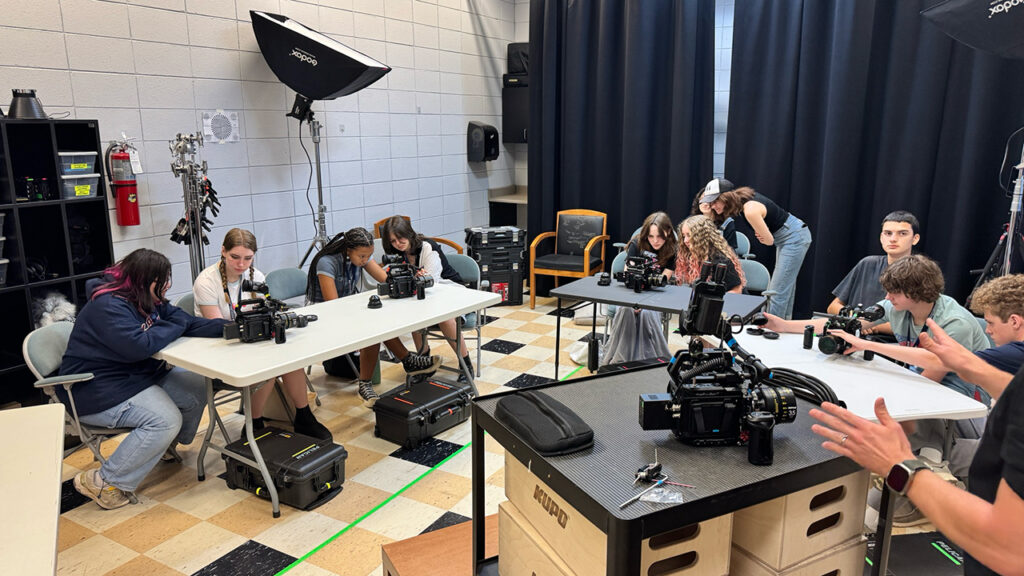 Students in a classroom examine various digital cameras