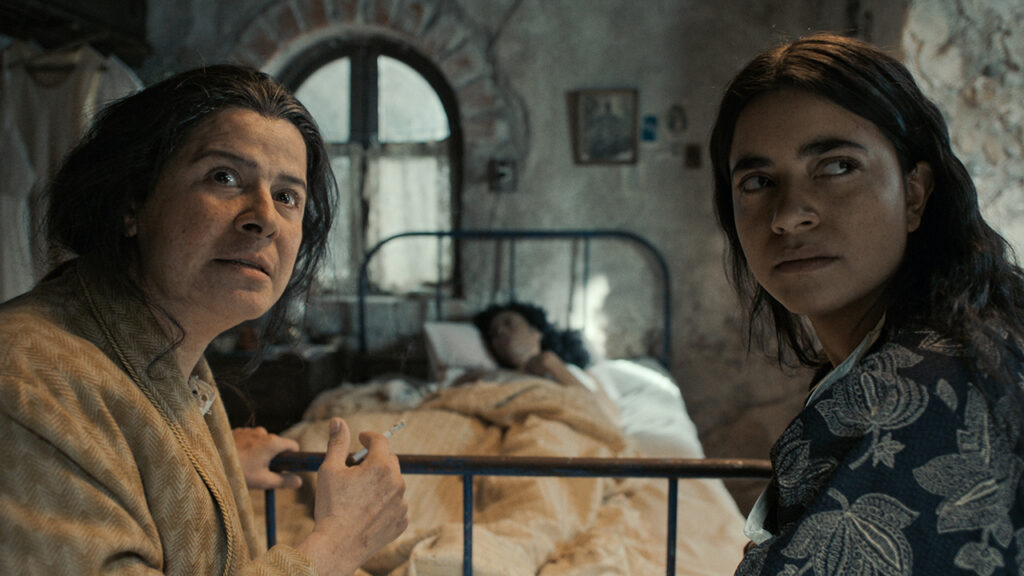 Two women sit at the foot of a patient's bed