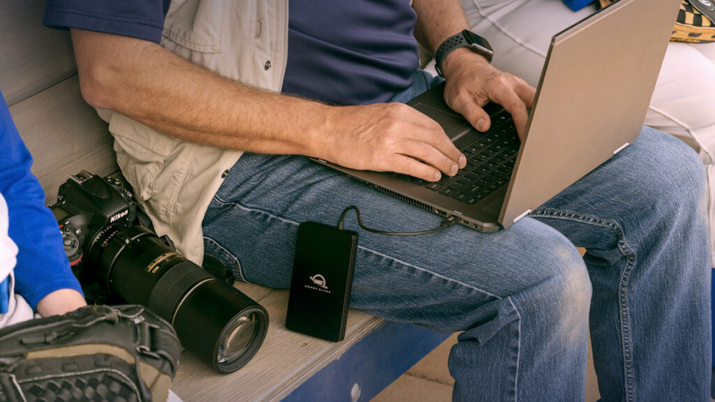 a man works on his laptop computer which is connected to an OWC 8TB Envoy Ultra