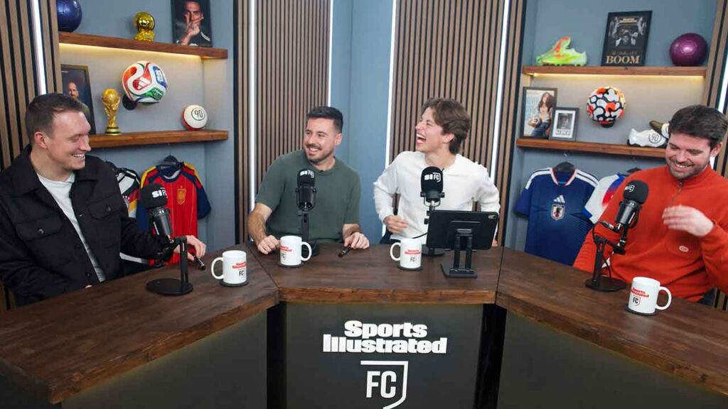 several men laugh while sitting at a table with microphones