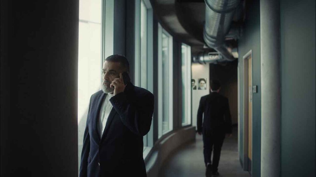 A man stands in a hallway staring out a window as he talks on his cell phone