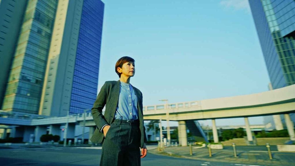A woman stands in a city staring off into the distance with her hand in her pocket