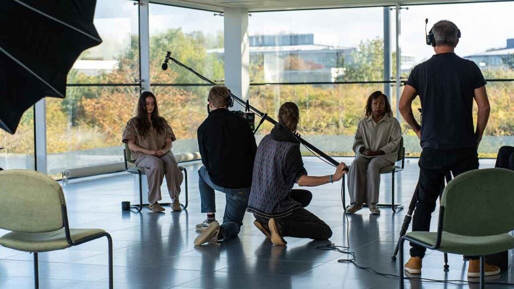 A woman sits on set while a man holds a boom