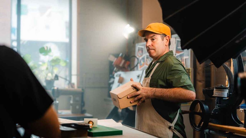 a man in a green shirt and yellow hat holds a box