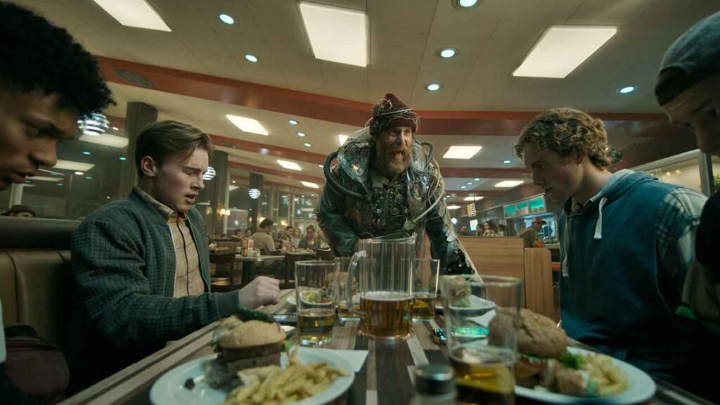 A movie scene where a man yells at a group of kids who sit eating in a diner