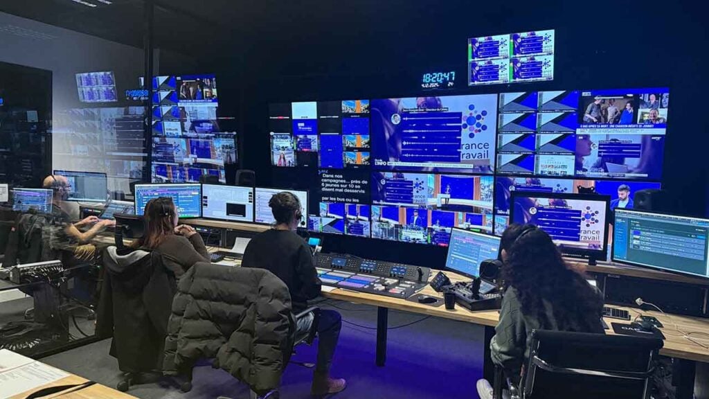 Several people sit in a production studio looking at many monitors