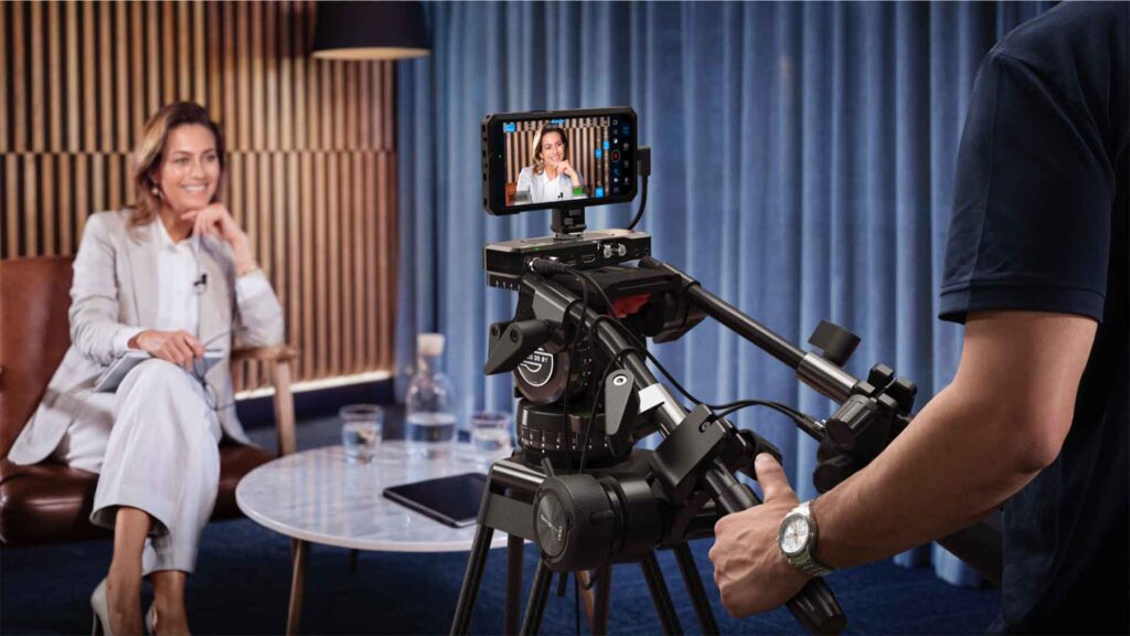 A smiling woman sits at a table in front of a Blackmagic camera