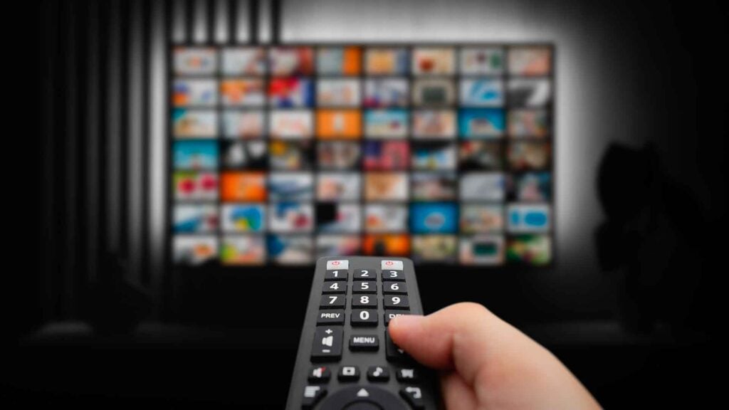 a person clicks a remote toward a television screen that displays a montage of streaming options
