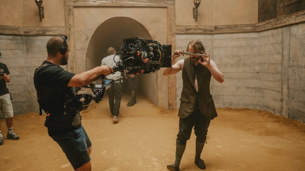 a cameraman films an actor who is holding a knife in front of their face