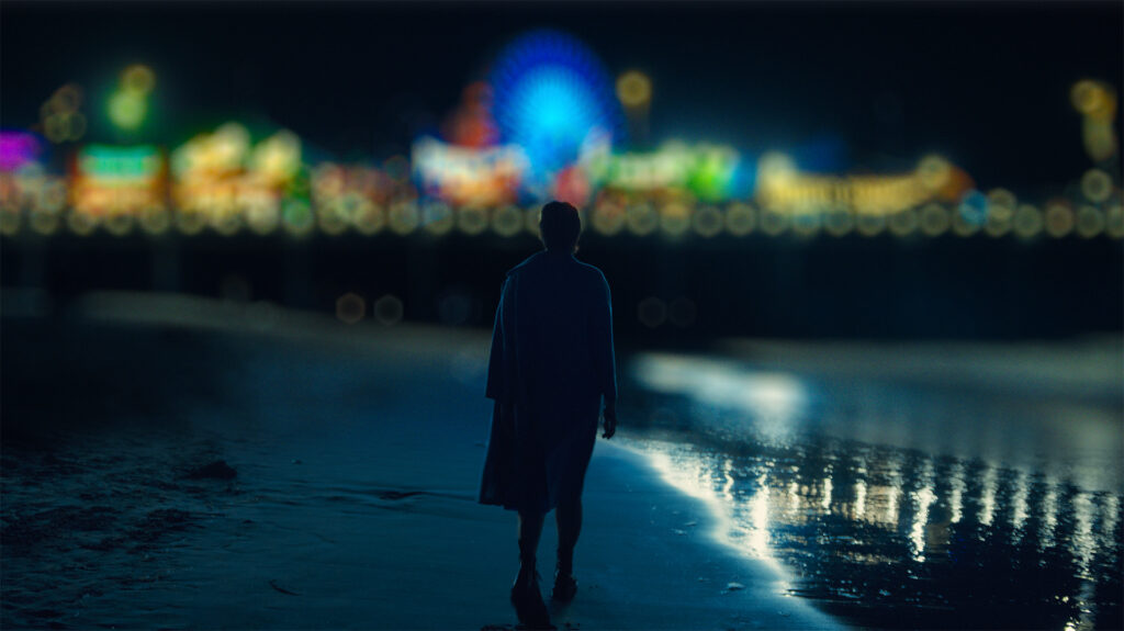 a man stares at the lights of a carnival in the distance