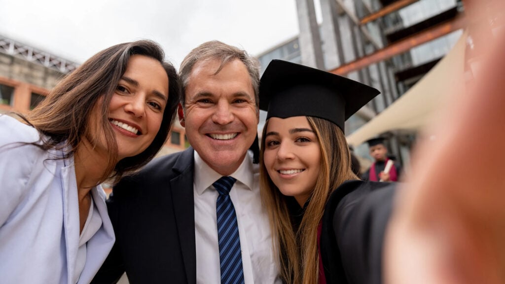 Two parents pose for a selfie with their graduating daughter