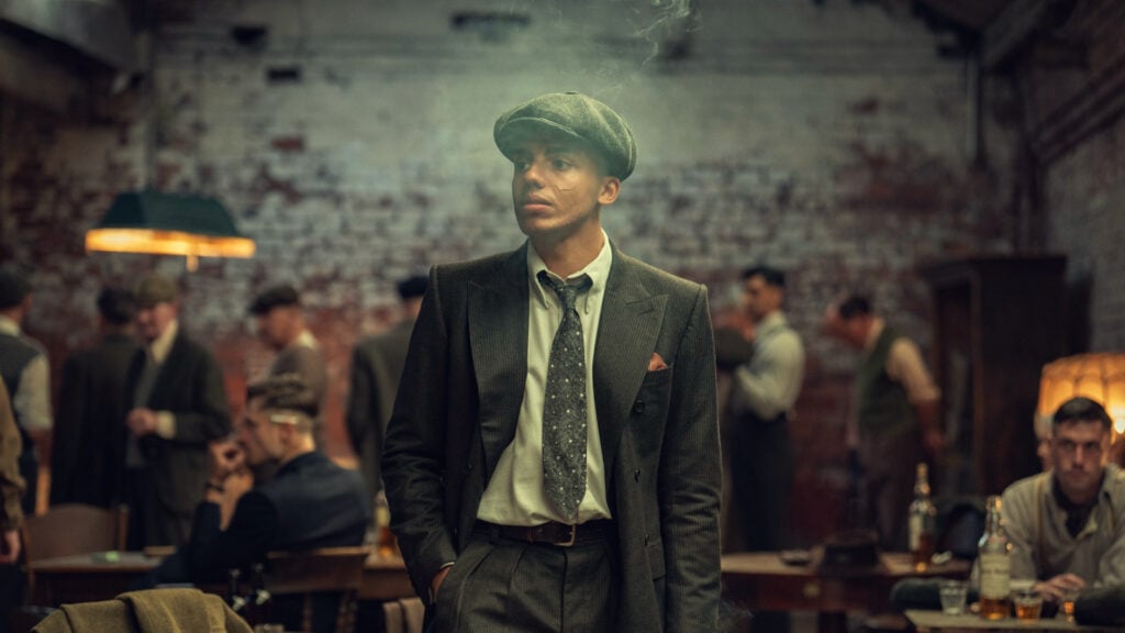 a man in a suit and hat walks through a smoky room