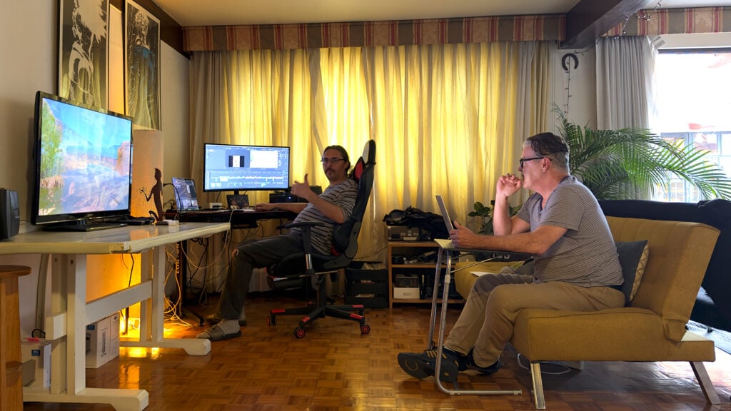 two men edit footage using computers and DaVinci Resolve software while sitting in a living room