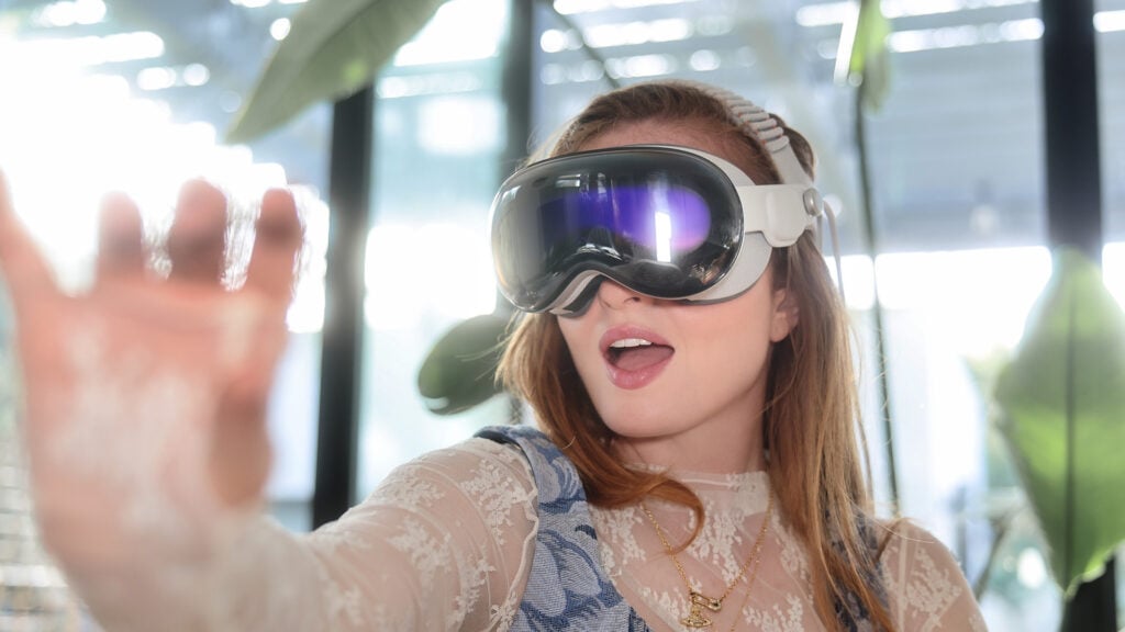 A woman in white wears a VR headset and reaches out into the air