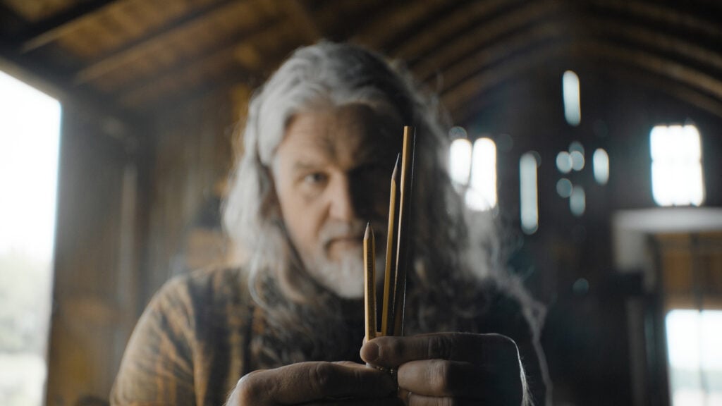 a grey haired man holds up several pencils