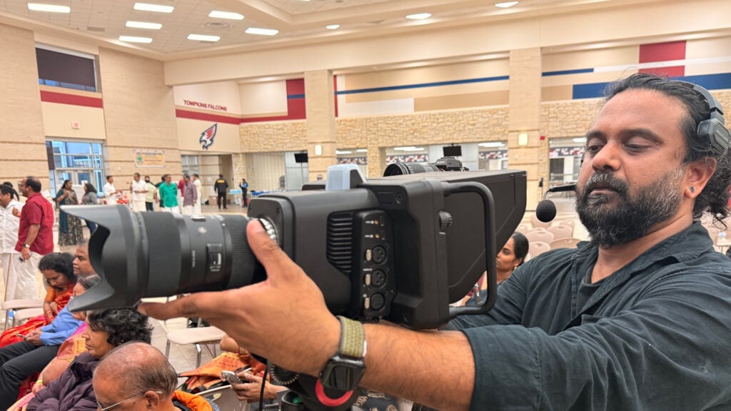 a man adjusts a Blackmagic camera at the Houston Tamil Sangam Literacy Competition