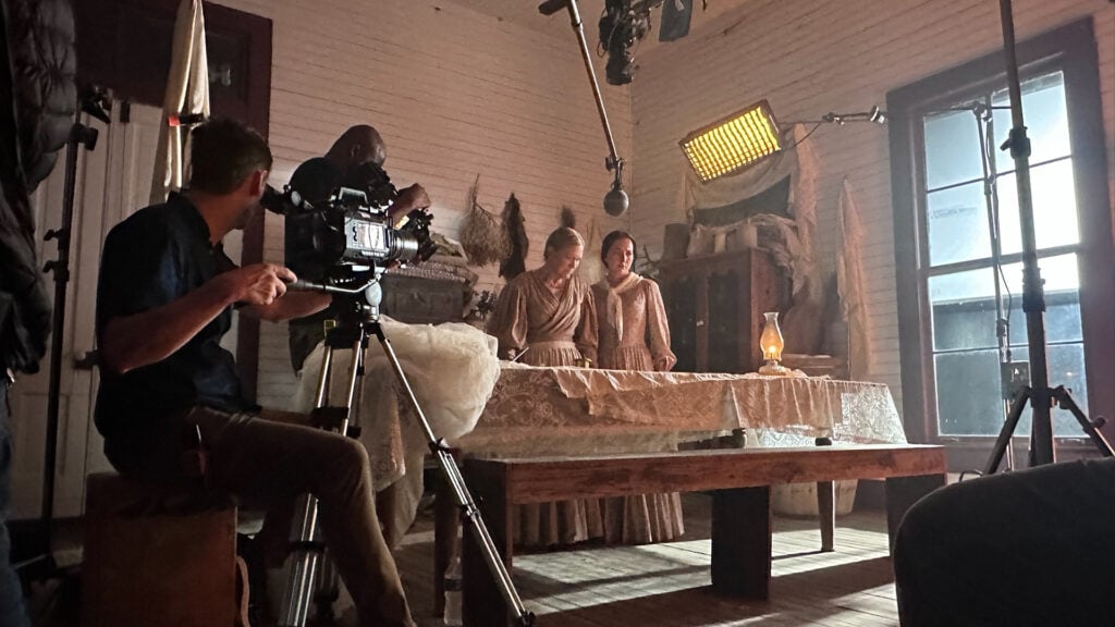 two cameramen film women in a period piece set in a Texas farmhouse