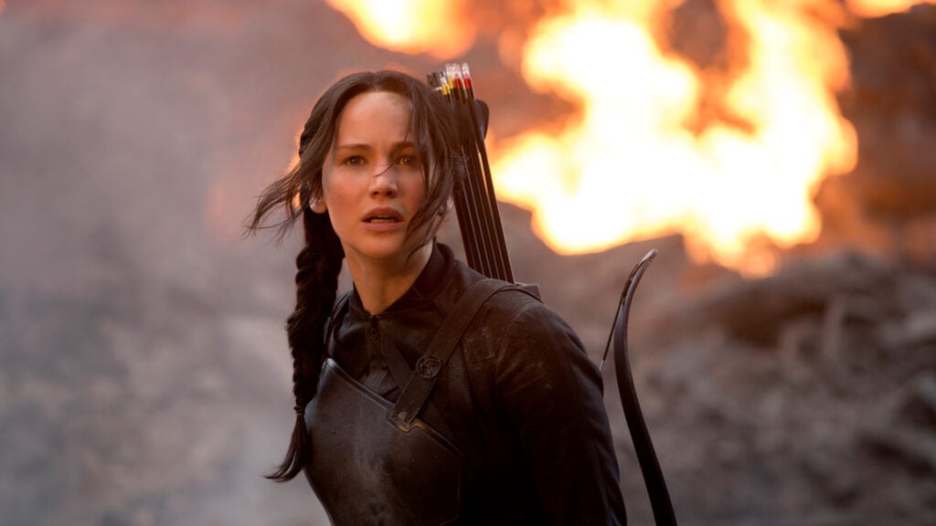 The character Katniss stands in a fiery landscape in the movie Hunger Games: Catching Fire