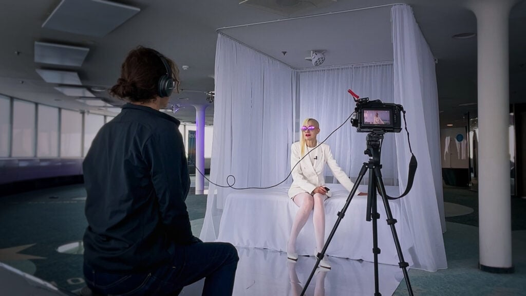 a photographer films a woman in white sitting on a white bench